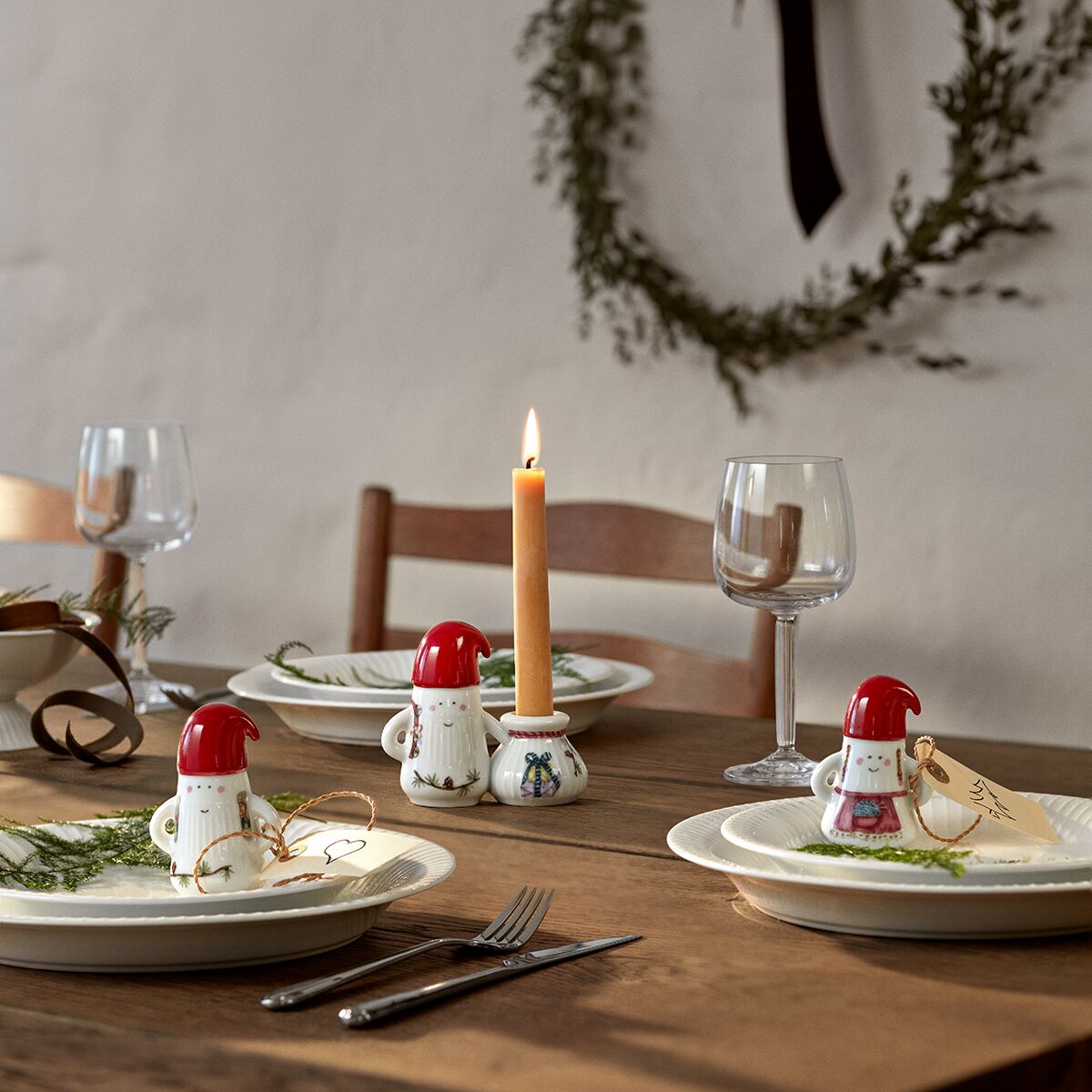 Eine festlich gedeckte Tafel mit Keramikfiguren in Form von Weihnachtsmännern der Serie »Hammershøi«, ergänzt durch einen Teller mit Tannenzweig, einem Weinglas und brennender Kerze. Die Szene vermittelt eine gemütliche, weihnachtliche Stimmung und eignet sich als Dekorations- oder Geschenkidee für die Advents- und Weihnachtszeit.