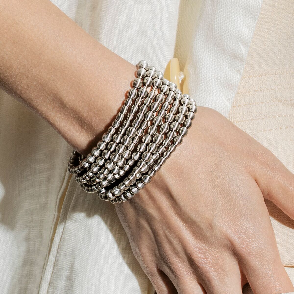 Nahaufnahme eines mehrreihigen silbernen Perlenarmbands am Handgelenk einer Person, aufgenommen vor neutralem Hintergrund. Das Armband wirkt elegant und modern, perfekt als modisches Accessoire oder Geschenk.