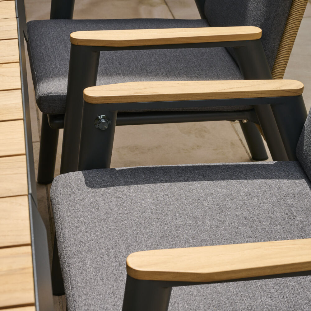 Sessel »Roma Dining Move« mit grauer Polsterung und Holzarmlehne, aufgestellt auf einer Terrasse. Sichtbar sind Details des Stuhldesigns und die Textur der Materialien.