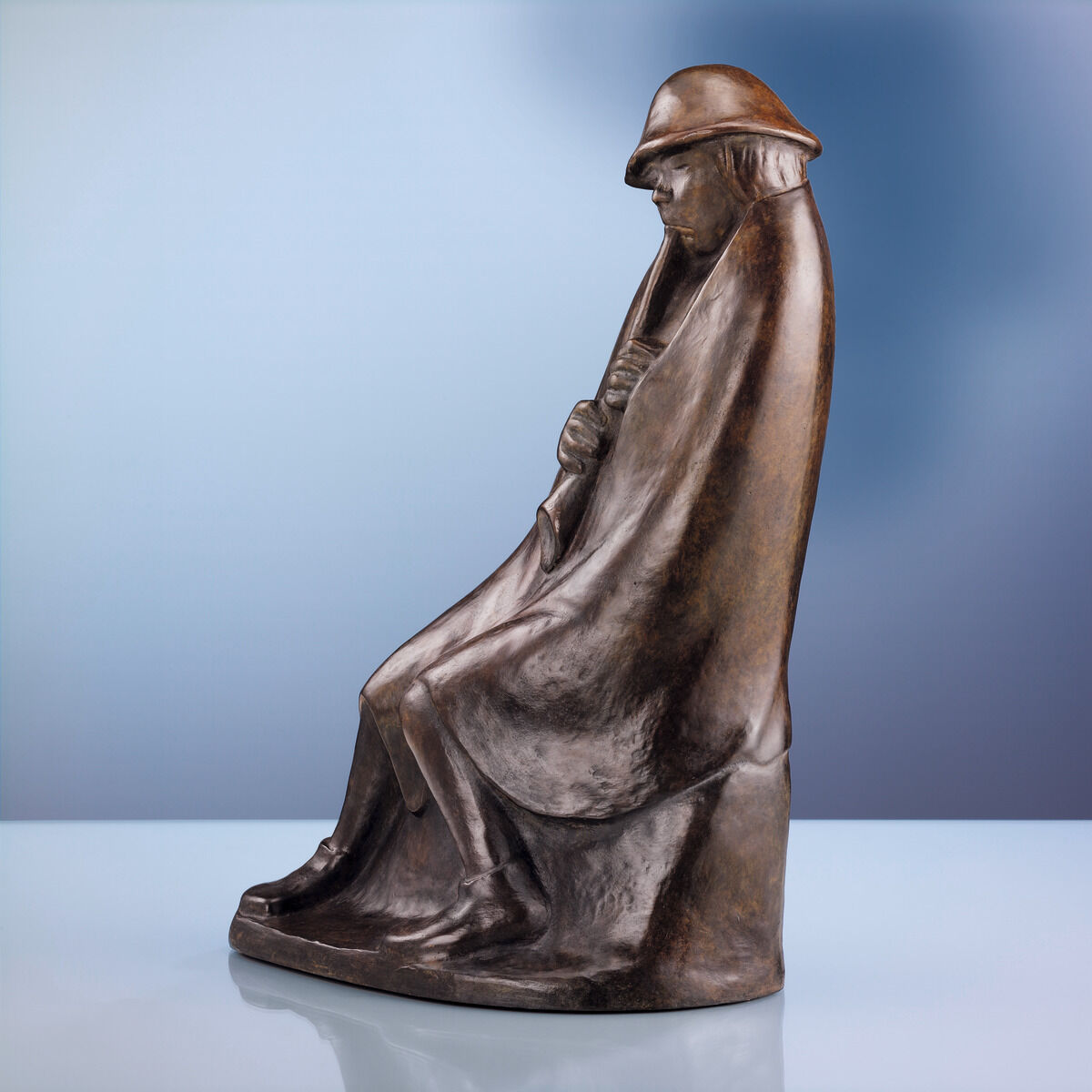 Eine Bronzeskulptur namens »Der Flötenbläser« von Ernst Barlach aus dem Jahr 1936. Die Skulptur zeigt eine in tiefem Braun gehaltene Figur eines auf dem Boden sitzenden Flötenspielers mit Umhang und Hut, vor einem sanft verlaufenden hellblauen und blauen Hintergrund.