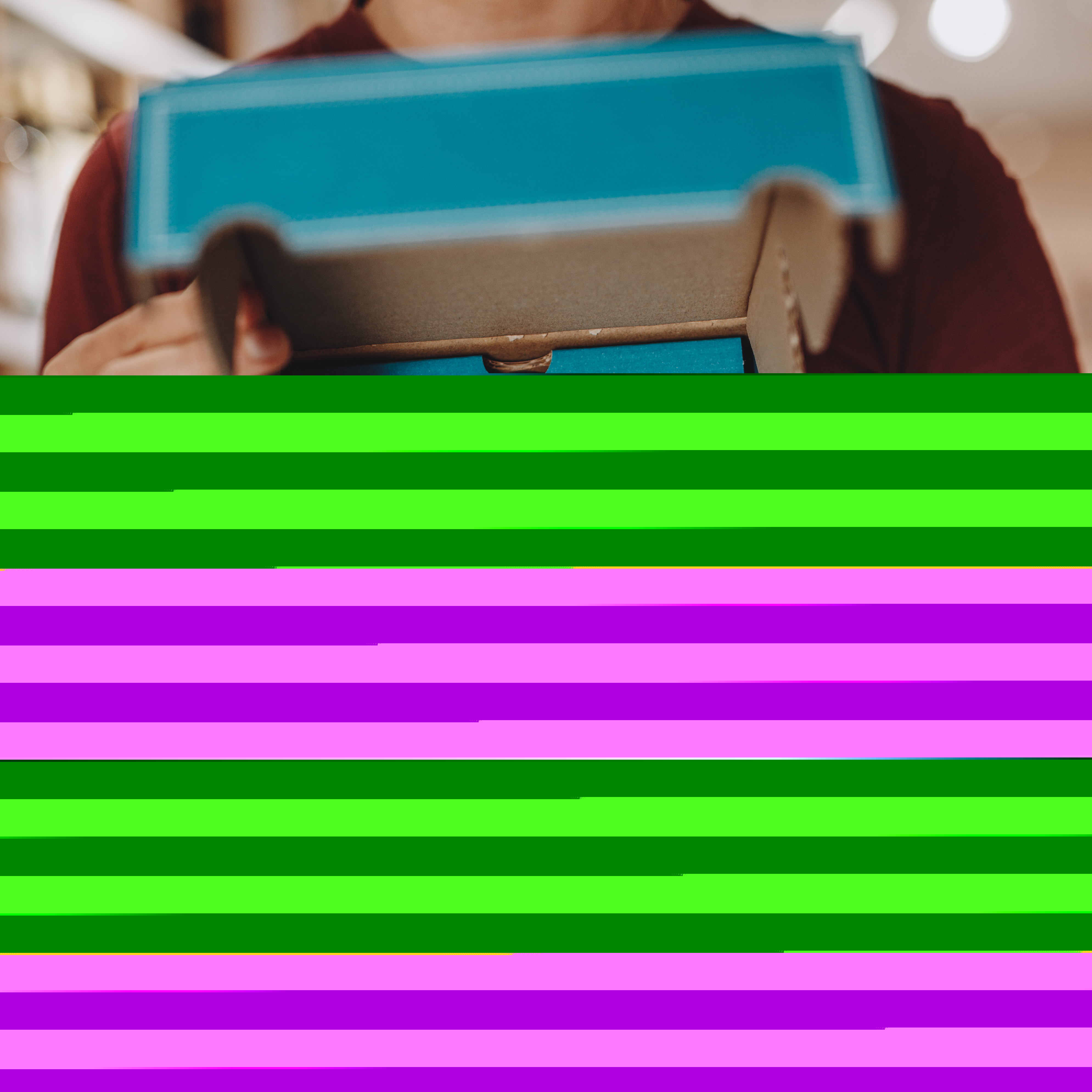 Eine Person hält eine blaue Geschenkbox mit weißem Herz und der Aufschrift 'Mit Liebe handgemacht' in den Händen. Die Box ist hochwertig verarbeitet und eignet sich als kulinarisches Präsent. Im Hintergrund sind Regale unscharf zu erkennen. Das Bild illustriert eine mediterrane Feinkost-Geschenkbox für besondere Anlässe.