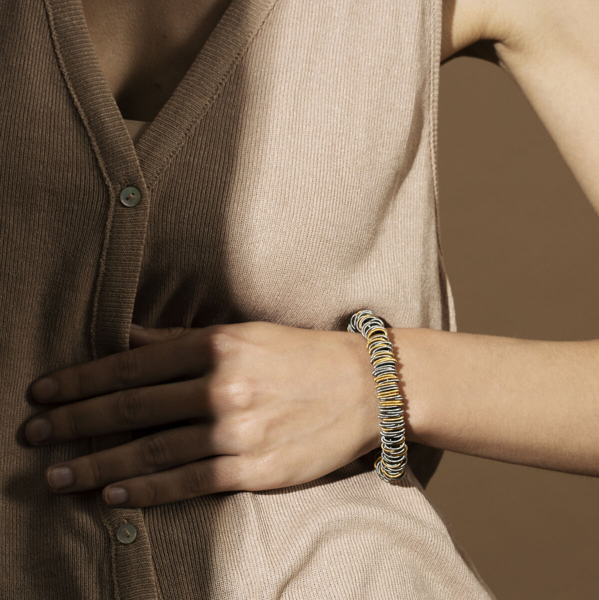 Person trägt ein beiges, ärmelloses Hemd und ein dekoratives Armband mit goldenen Akzenten am Handgelenk.