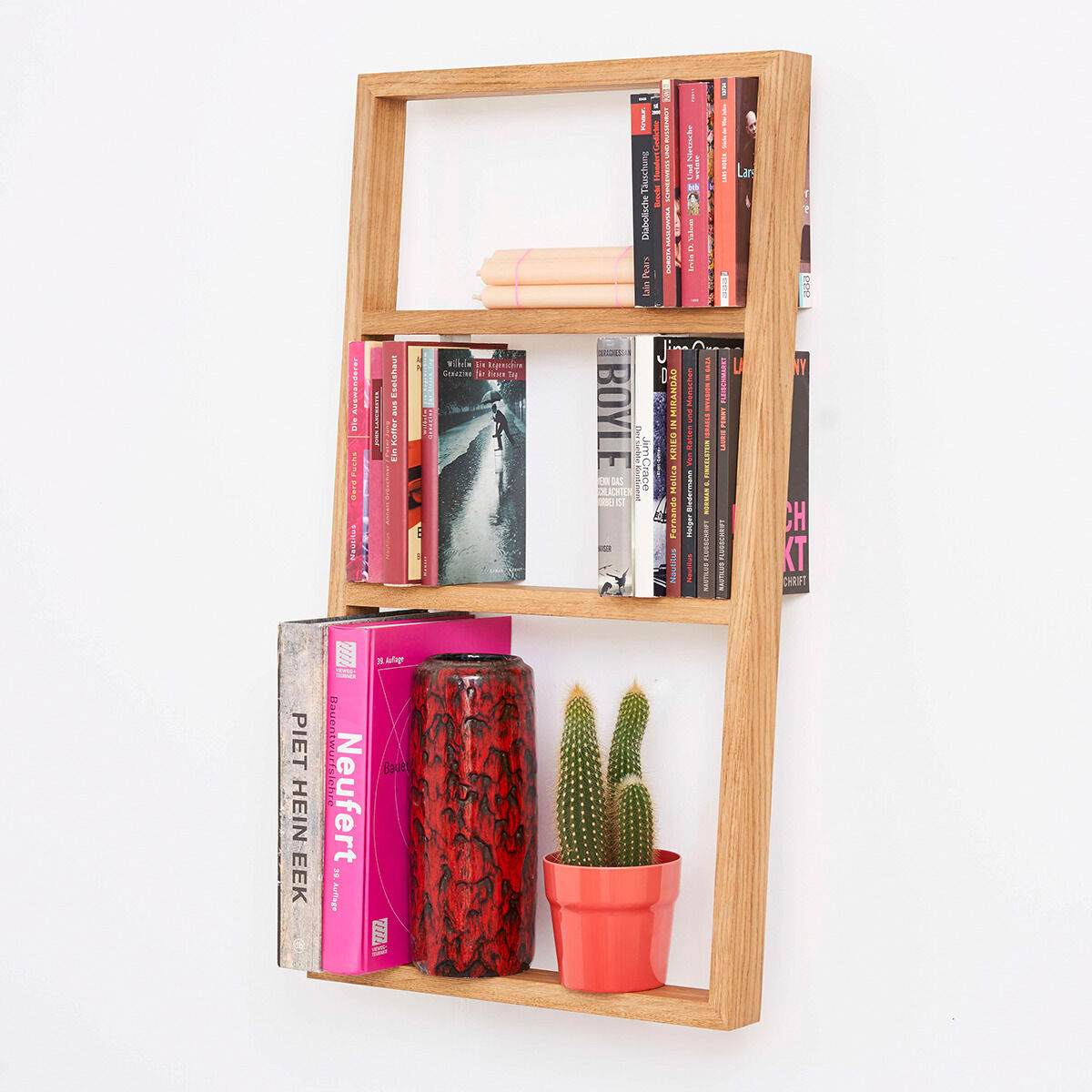 Wandregal aus Holz mit Büchern, zwei Kerzen, einem Kaktus in einem roten Topf, und einer dekorativen Vase. Modernes Design für unterschiedliche Wohnräume.