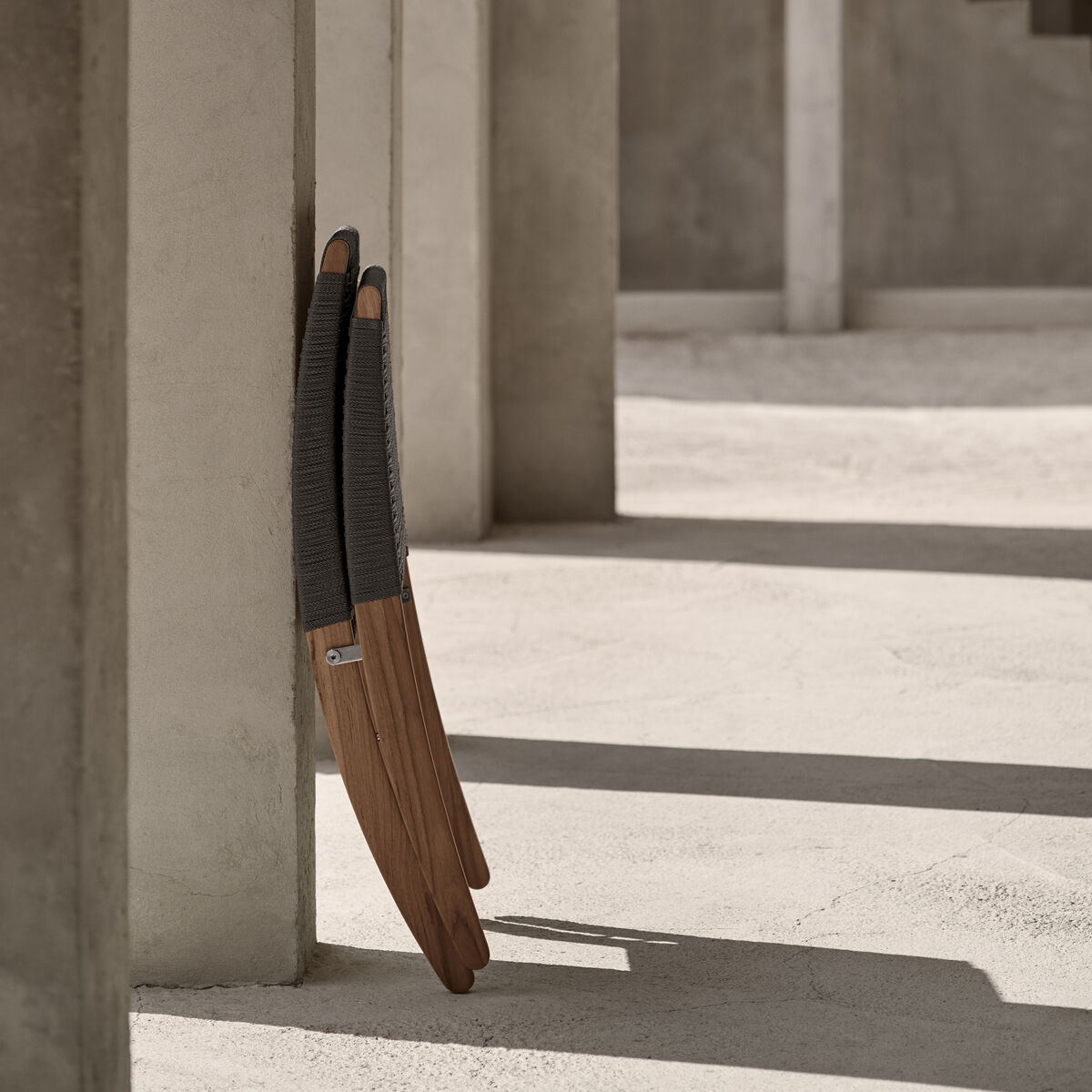 Zwei übereinander gestapelte Outdoor-Stühle der Marke 'MG501 Cuba Chair' aus Holz und geflochtenem Material stehen in einer modernen, betonierten Umgebung mit Säulen und Treppen im Hintergrund.