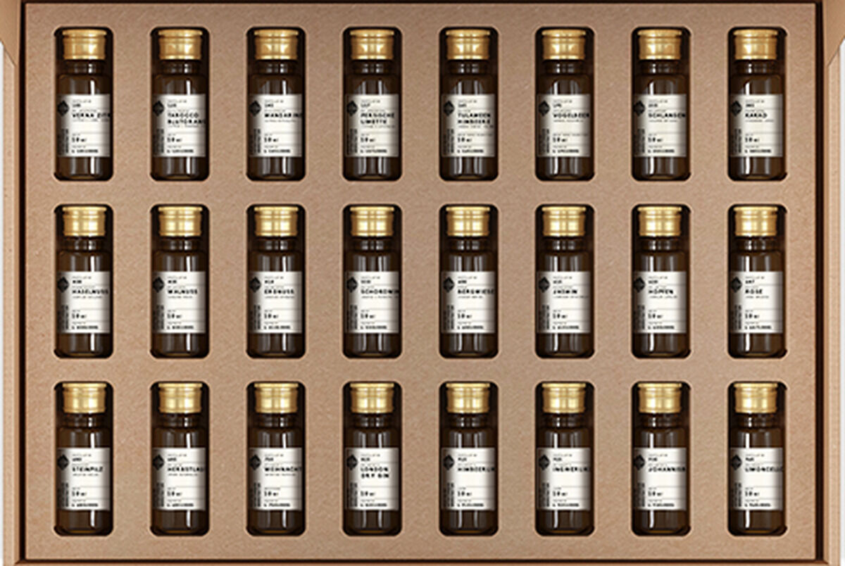 Eine geöffnete Adventskalender Tastingbox aus braunem Karton, gefüllt mit kleinen Flaschen, jede mit einem schwarzen Etikett und goldfarbenem Verschluss. Neben der geöffneten Box steht eine geschlossene, sichtbare Außenseite.