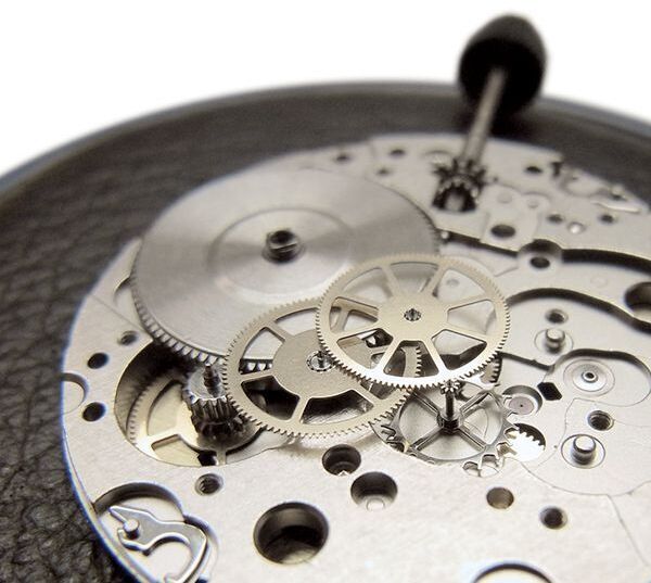 Mechanisches Uhrwerk der Uhrenedition ZEIT 1 aus Edelstahl mit komplexen Zahnrädern und detailliertem Design. Hochwertige Verarbeitung und stilvolles Aussehen.