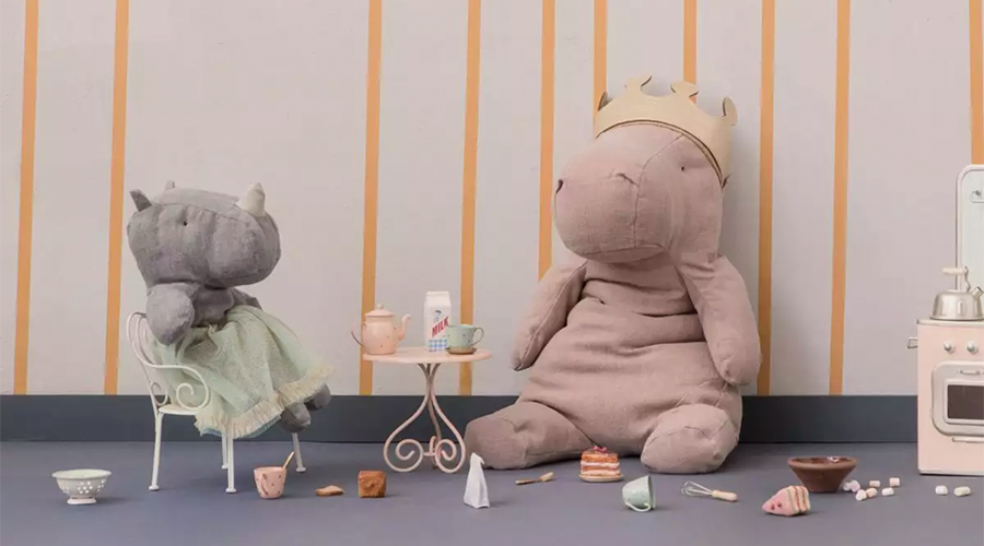 Zwei große Kuscheltiere, ein Nilpferd mit Krone und ein Nashorn mit grünem Tuch, sitzen in einem Kinderzimmer mit Spielzeug und Teegeschirr