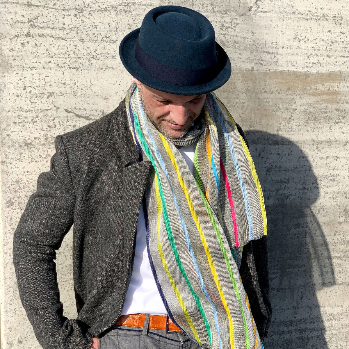 Ein länglicher Leinenschal mit naturweißer Grundfarbe liegt locker gefaltet. Quer verlaufen unregelmäßig bunte Streifen aus glänzender Seide in Rot, Grün, Blau, Gelb und Orange. Der Stoff wirkt leicht, luftig und hochwertig, mit feiner Struktur und dezentem Glanz.