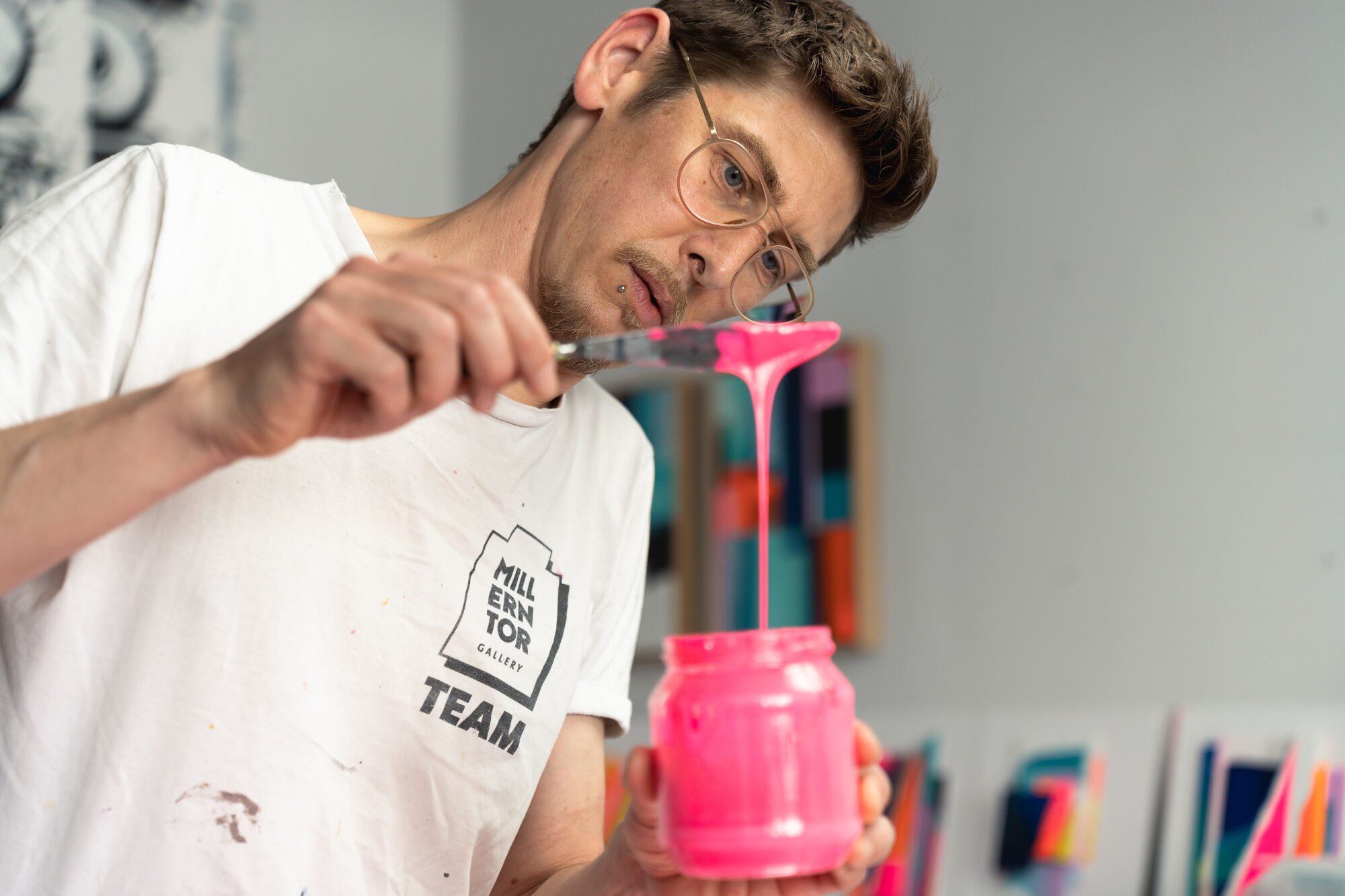 Person gießt pinke Farbe aus einem Spatel in ein Glas, trägt weißes T-Shirt mit 'Millen Tor' und 'Team' Schriftzug