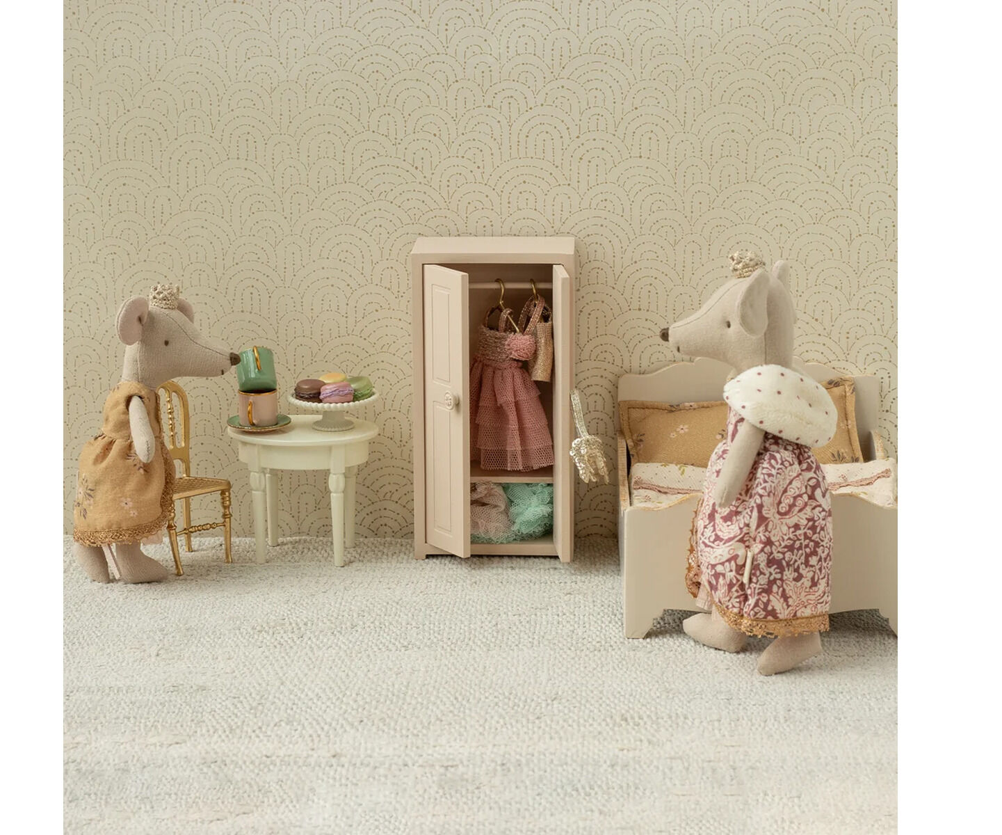 Drei detailreich gestaltete Stoffmäuse der Marke Maileg stehen in einem Miniaturzimmer mit Vintage-Tapete. Eine sitzt an einem weißen Tisch mit Kuchen, eine steht an einem geöffneten Schrank mit Kleidung, die dritte trägt ein Krönchen und steht an einem Bett.