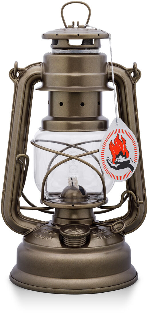 Eine bronzefarbene Sturmlaterne mit Glasgehäuse und einem Henkel oben. Die Laterne hat ein Etikett mit einem Flammensymbol. Sie steht auf einem weißen Hintergrund.