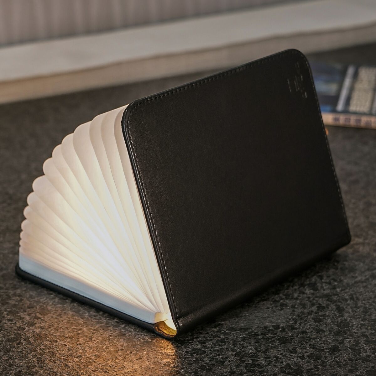 Ein Smart Booklight aus schwarzem Leder, das auf einem Tisch liegt, mit einer leuchtenden Seite, die wie eine aufgeschlagene Buchseite aussieht.