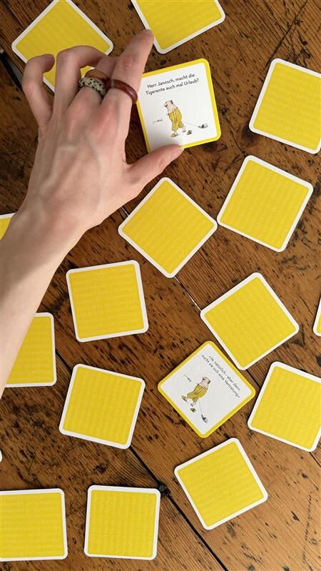 alt="Memo-Spiel auf einem Tisch ausgebreitet mit einer Hand im Bild, die eine Karte zieht"