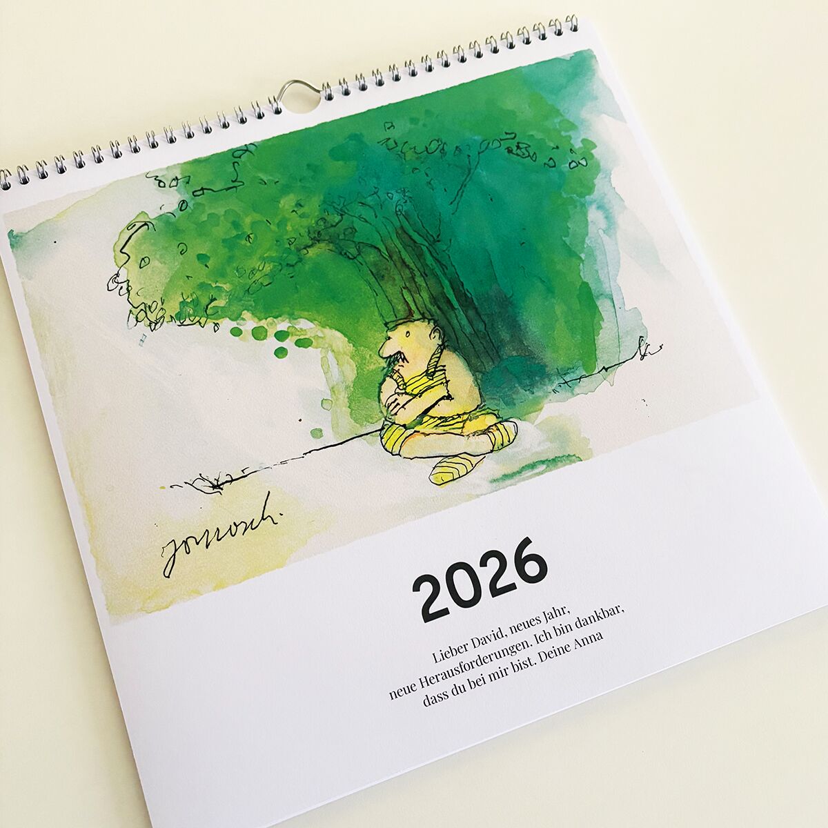 Kalender mit dem Titel 'Wondrak-Kalender 2026', abgebildet ist eine künstlerische Illustration einer sitzenden, nachdenklichen Figur unter einem Baum, umgeben von grünen Aquarellfarben. Darunter steht das Jahr 2026 sowie ein kurzer humorvoller Spruch.
