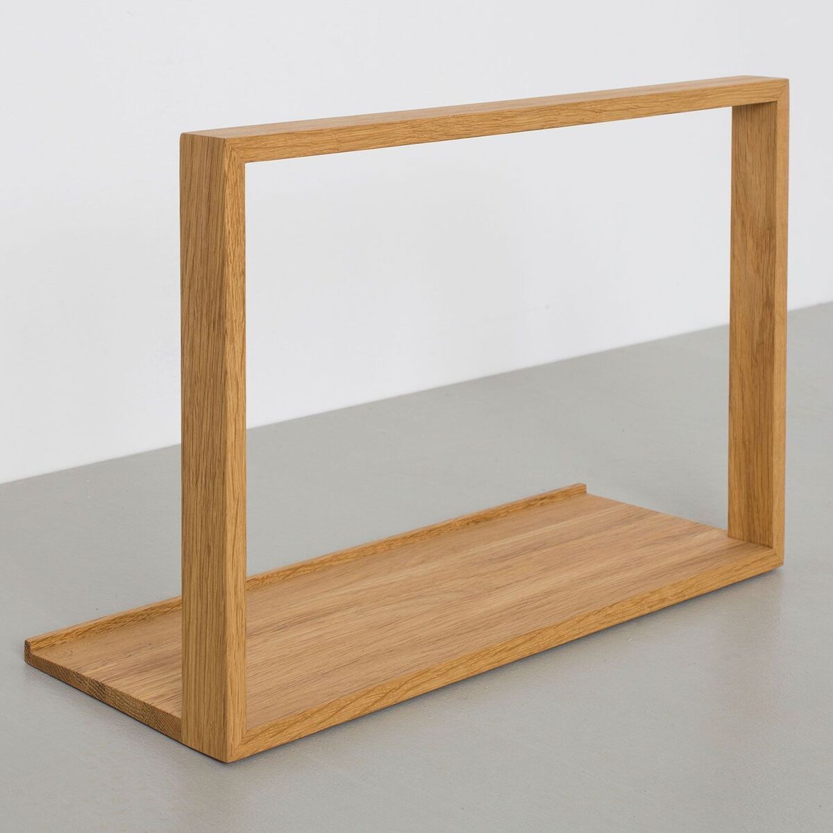 Holzfarbener, minimalistischer Plattenständer »B-Seite« auf einem hellgrauen Untergrund vor einer weißen Wand.