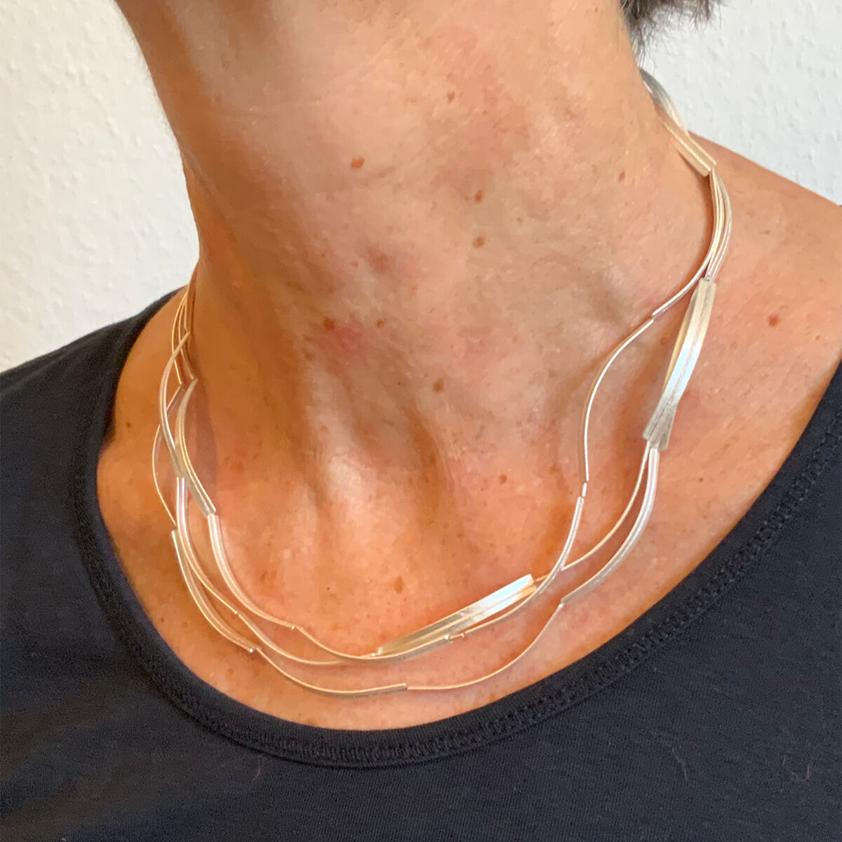 Eine stilvolle Silberkette mit mehreren geschwungenen Strängen wird um den Hals getragen. Die Kette hat ein schlichtes und modernes Design.