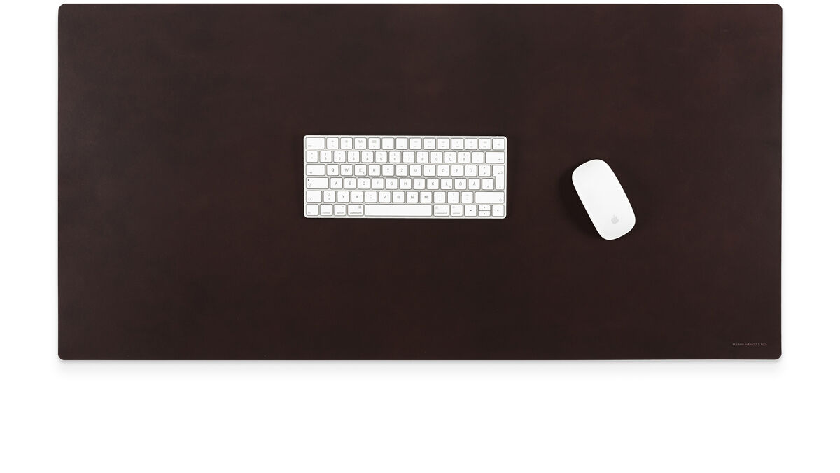 Braune Schreibtischunterlage aus Lederoptik, darauf eine weiße Tastatur und eine weiße Maus, alles auf einem modernen, minimalistischen Arbeitsplatz arrangiert.