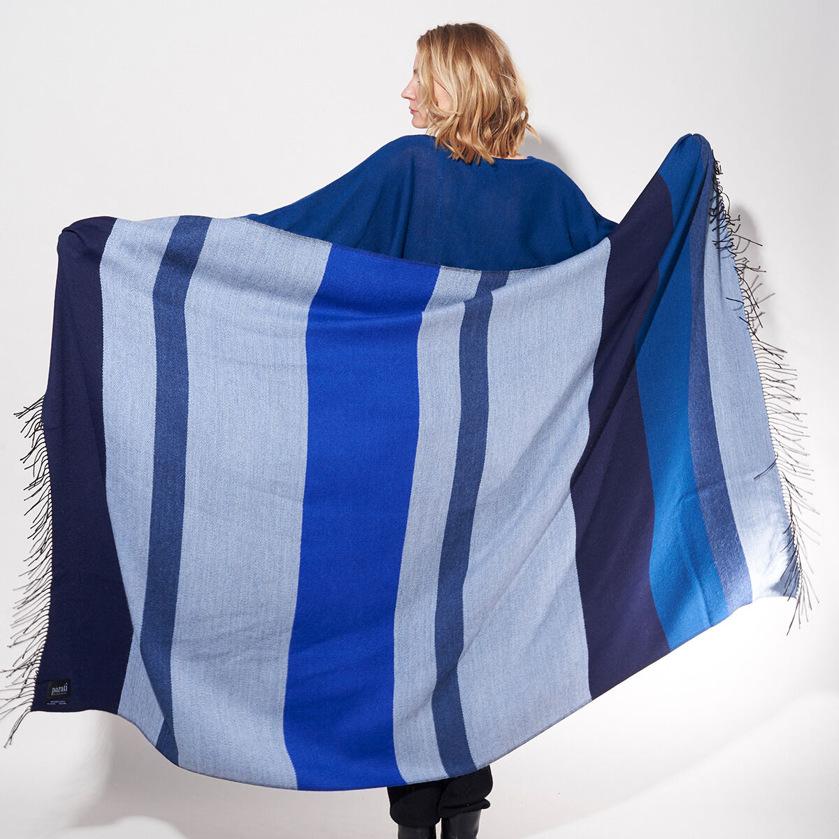 Eine Person trägt ein Cape mit blauen und weißen Streifen aus der ZEIT-Jubiläumsedition »Shades of Blue«. Der Cape ist in verschiedenen Blautönen gehalten und wirkt warm und gemütlich.