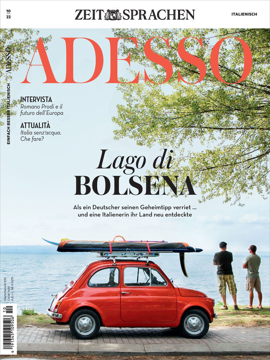 Titelseite der Zeitschrift 'Adesso' Ausgabe 10/2022. Ein roter Fiat 500, auf dem Surfboards befestigt sind, steht vor einem See (Lago di Bolsena) mit Bäumen im Hintergrund. Zwei Personen stehen nah am Wasser. Oben sind die Titel und Hauptthemen der Ausgabe geschrieben.