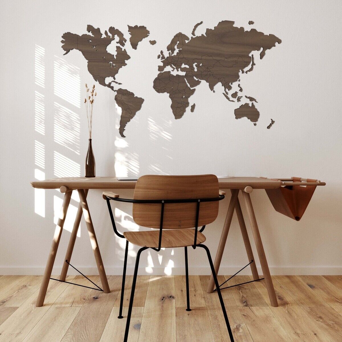 Ein stilvolles Arbeitszimmer mit einer selbstklebenden Weltkarte aus Holz an der Wand, einem Holzschreibtisch mit einer schwarzen Stuhlfläche und einer Holzvase mit Zweigen, die im Sonnenlicht steht.