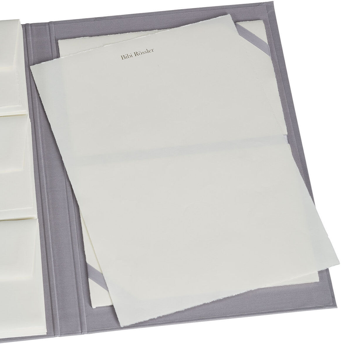 Eine graue Briefpapiermappe enthält edles Büttenpapier, ordentlich gestapelt. Die Mappe hat mehrere Fächer und das Papier ist von hoher Qualität.