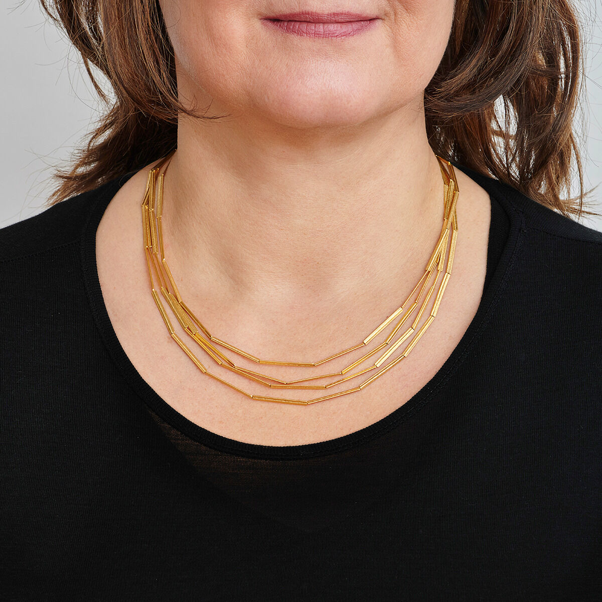 Eine Frau trägt eine goldplattierte Halskette mit Streifenmuster, die auf einem schwarzen Oberteil liegt.