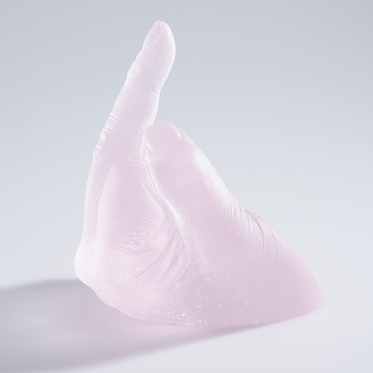 Eine rosa Glas-Skulptur in Form einer aufrechten menschlichen Hand, die transparent und minimalistisch gestaltet ist.