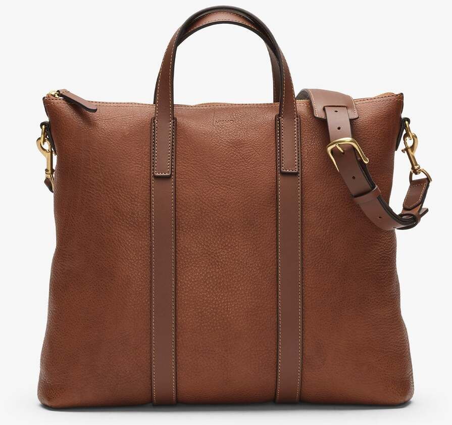 Die Ledertasche »MATE« von Mismo ist eine hochwertige, braune Ledertasche mit goldenen Beschlägen. Sie verfügt über zwei Tragegriffe und einen abnehmbaren Schulterriemen.