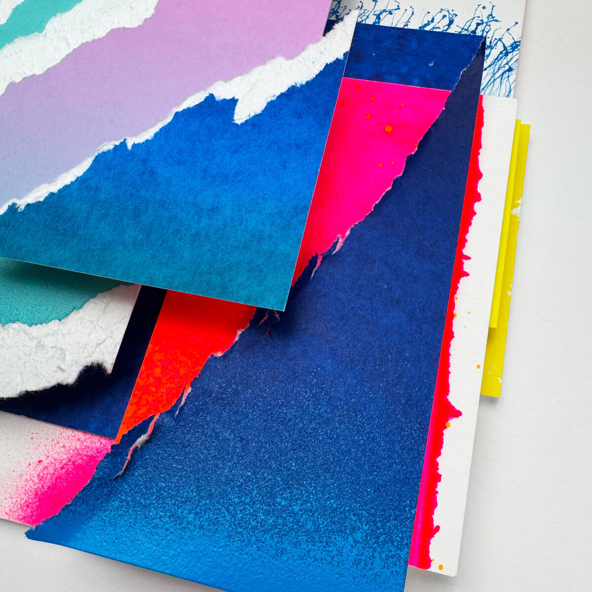 Mehrschichtige Collage aus farbigem Papier mit rauen, gerissenen Rändern in Blau, Pink, Weiß und Violett. Die Schichten überlappen teils diagonal, kräftige Farben, teils Sprüh-Effekte. Gerahmt, modern, abstrakt, mit dynamischer Tiefenwirkung.