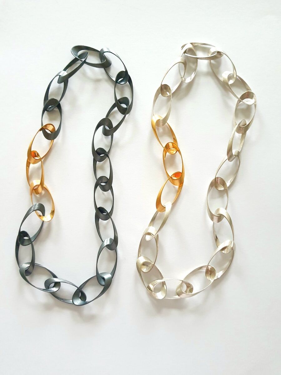 Zwei Kolliers aus Silber und Gold, jeweils mit einem modernen, verschlungenen Design. Eins ist komplett silber, das andere kombiniert Silber und Gold.