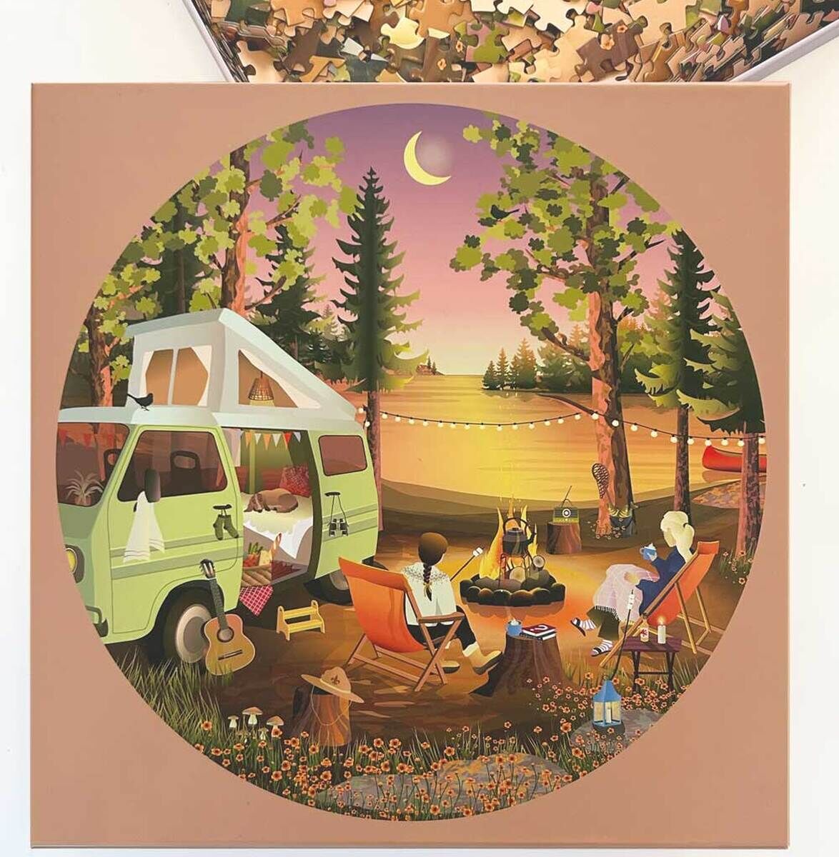 Ein Puzzle mit dem Titel »Van Life«, das eine entspannte Szene im Freien zeigt. Zwei Personen sitzen auf Campingstühlen um ein Lagerfeuer in einem Wald, mit einem grünen Wohnmobil im Hintergrund und einem See in der Ferne. Der Abendhimmel ist in Rosa- und Violetttönen gefärbt.