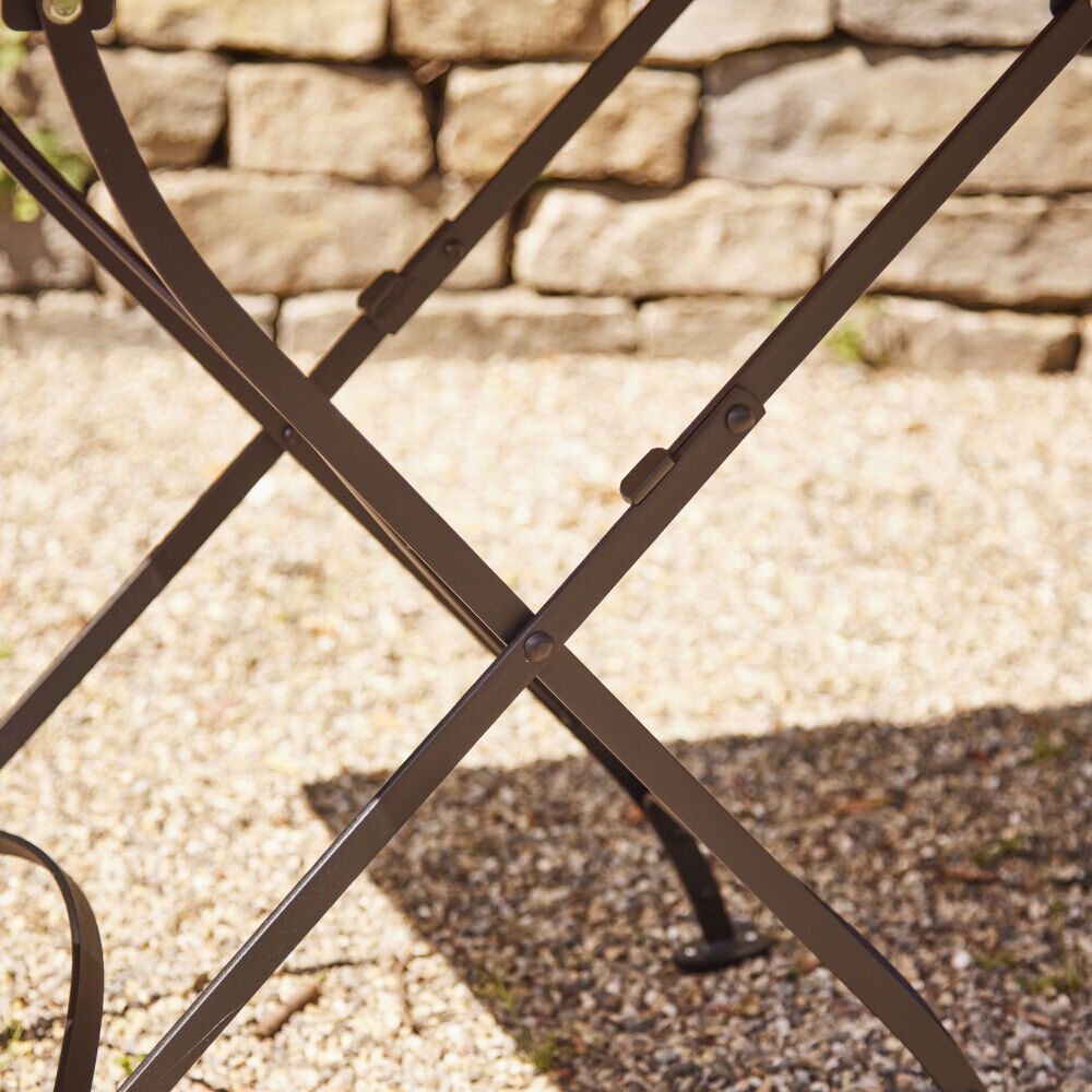 Nahaufnahme eines zusammenklappbaren Holztischs mit Metallrahmen, auf einer Terrasse mit Natursteinmauer im Hintergrund.