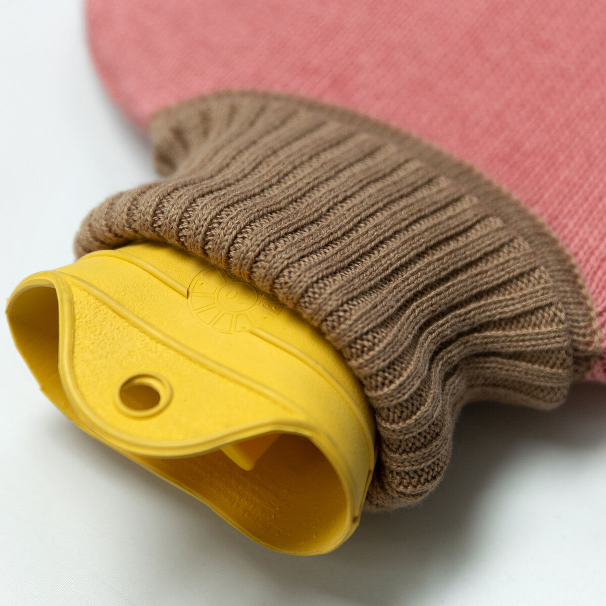 Detailansicht der SUITE702 Wärmflasche 2L Pink: Die Flasche besitzt einen gelben Verschluss aus Latex, umhüllt von einem gestrickten, beigebraunen und rosafarbenen Baumwollüberzug. Der weiche Überzug schützt vor direktem Kontakt mit der Wärmeflasche. Liegt auf einer weißen Oberfläche.