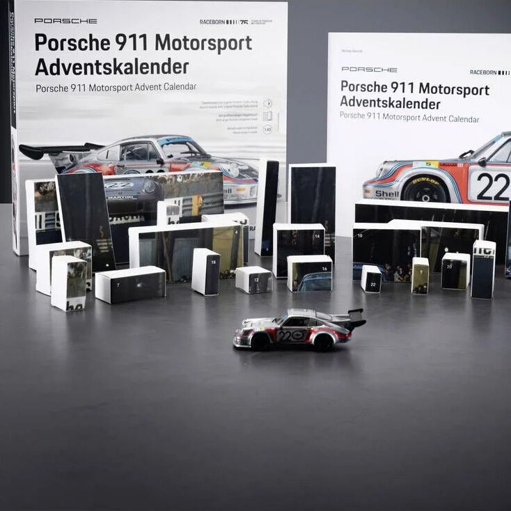 Der Adventskalender »FRANZIS 67275 - Porsche 911 Turbo Motorsport Adventskalender 1:43« von ZEIT Buchhandlung zeigt zwei große Verpackungen mit Porsche-Rennautodesign, viele kleine Geschenkboxen und ein silbernes Modellauto des Porsche 911 Turbo (1:43) auf einer grauen Fläche.