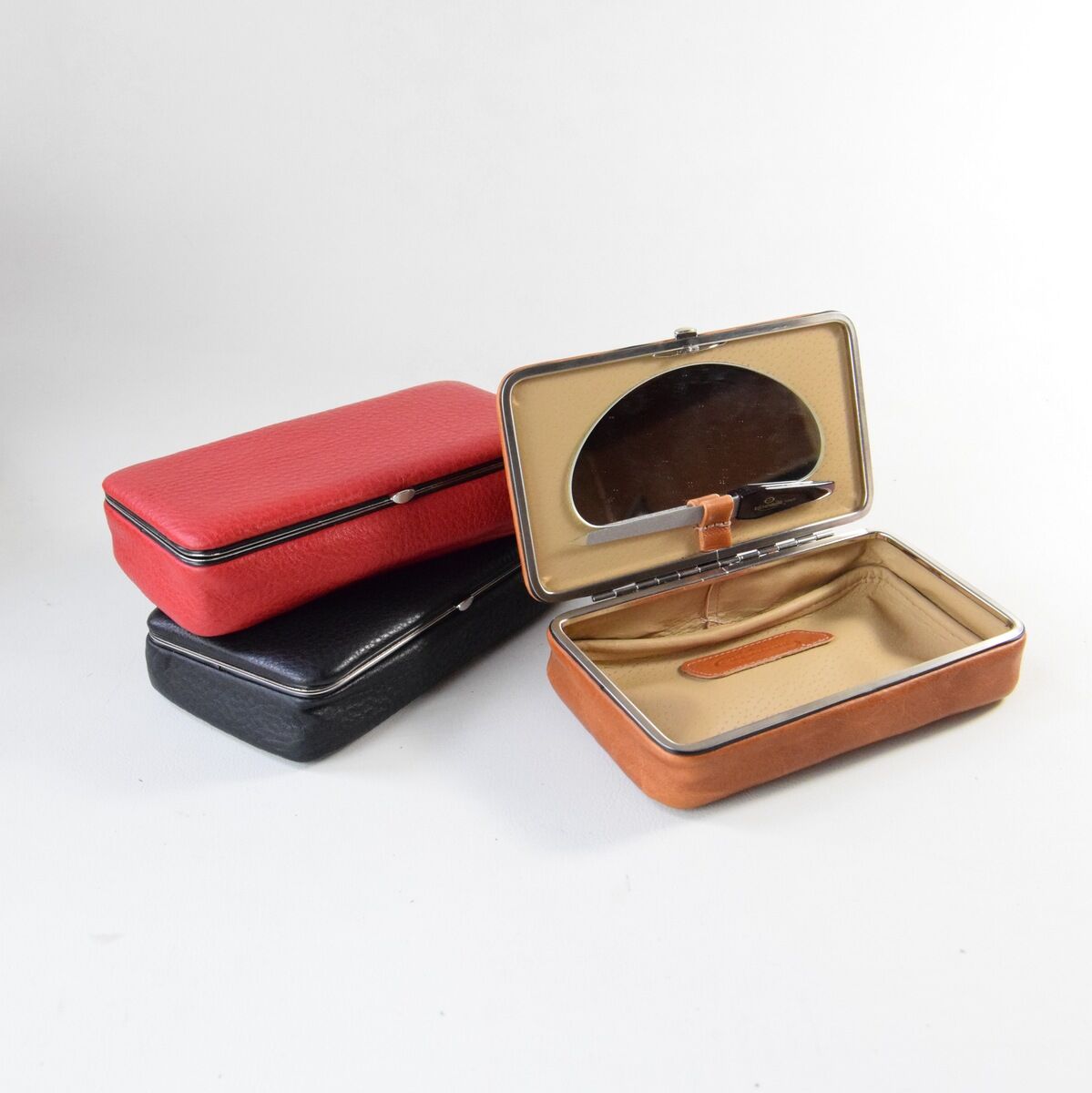 Mehrere Utensilienboxen aus Leder in verschiedenen Farben, einschließlich rot, schwarz und braun. Eine der Boxen ist geöffnet und zeigt ein beiges Innenfutter mit Fächern.