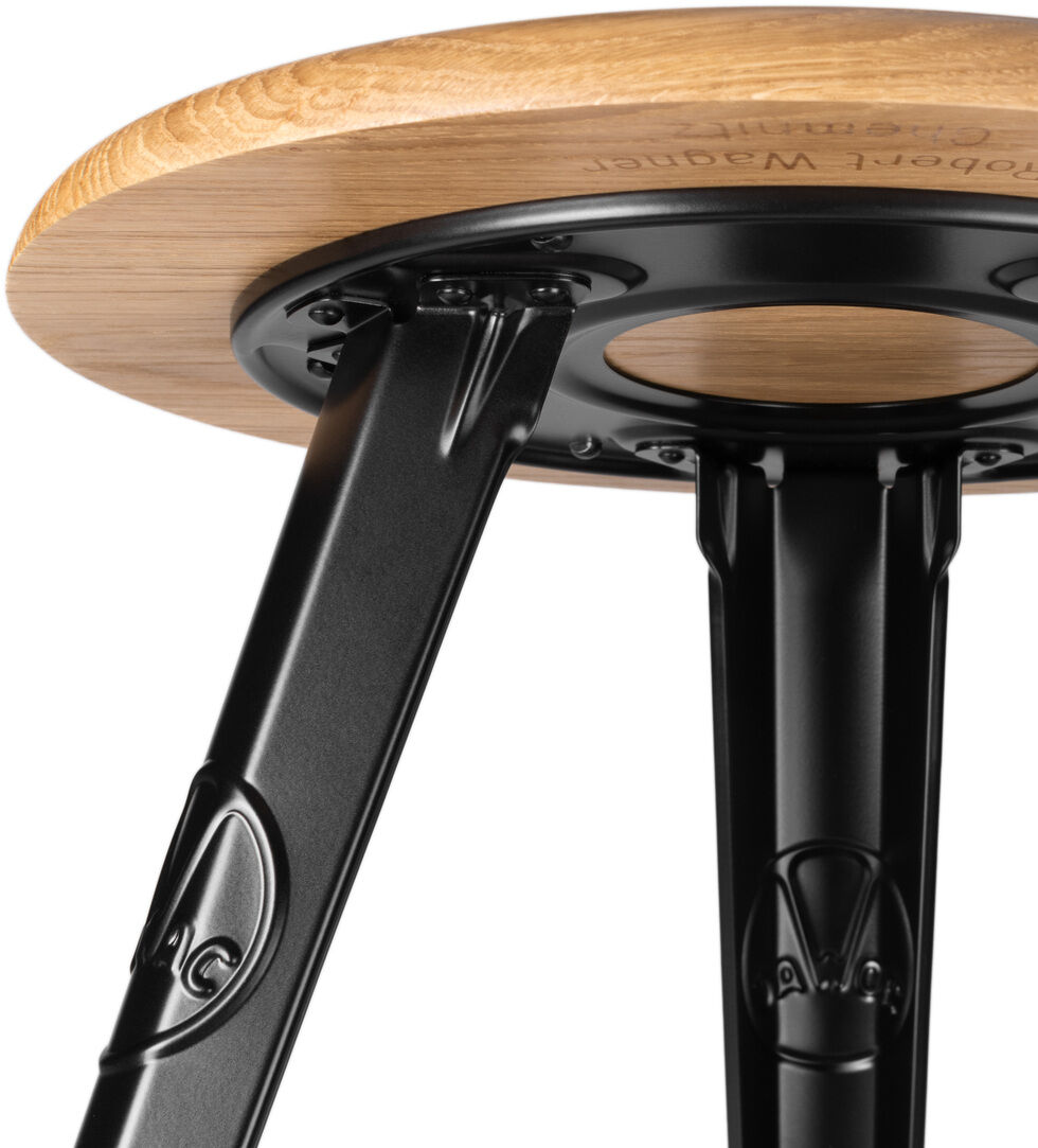 Ein Hocker mit runder Sitzfläche aus Eichenholz und mattschwarzen Metallbeinen im industriellen Stil.