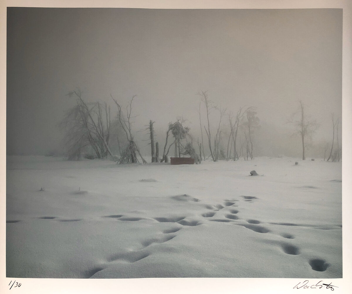 Ein künstlerisches Foto von Wackerbarth mit dem Titel »Kahler Asten 2016«. Das Bild zeigt eine verschneite Landschaft mit Bäumen, die im Nebel verschwinden. Fußspuren führen auf eine Kiste in der Mitte des Bildes zu und der gesamte Hintergrund ist in den Farben Weiß, Grau und Schwarz gehalten.
