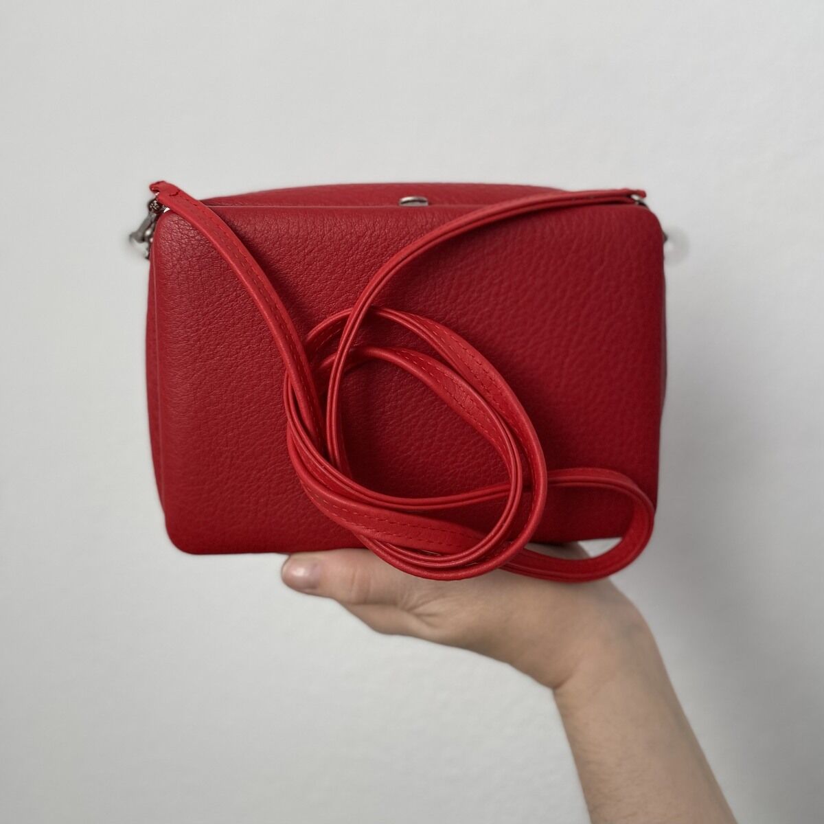 Eine rote Schultertasche aus Leder mit einer Hand, die sie vor einem weißen Hintergrund hält.