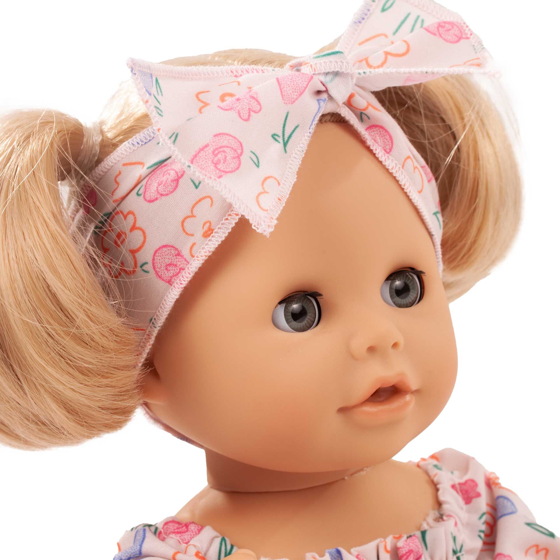 Abgebildet ist eine Badepuppe mit einem bunten Blumen-Kopftuch und Kleid. Die Puppe hat runde Wangen und einen freundlichen Gesichtsausdruck. Sie ist für Kinder und als Spielzeug für Wasser und Schlafen geeignet.