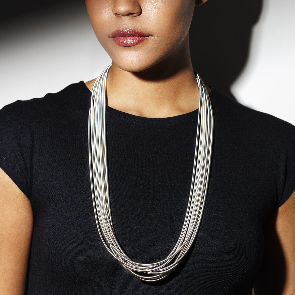 Frau mit schwarzem Oberteil trägt ein modernes, silberfarbenes Collier mit mehrfach verdrehten Strängen, fotografiert vor einem neutralen Hintergrund. Das Schmuckstück hebt sich stilvoll ab und wirkt elegant sowie zeitlos.