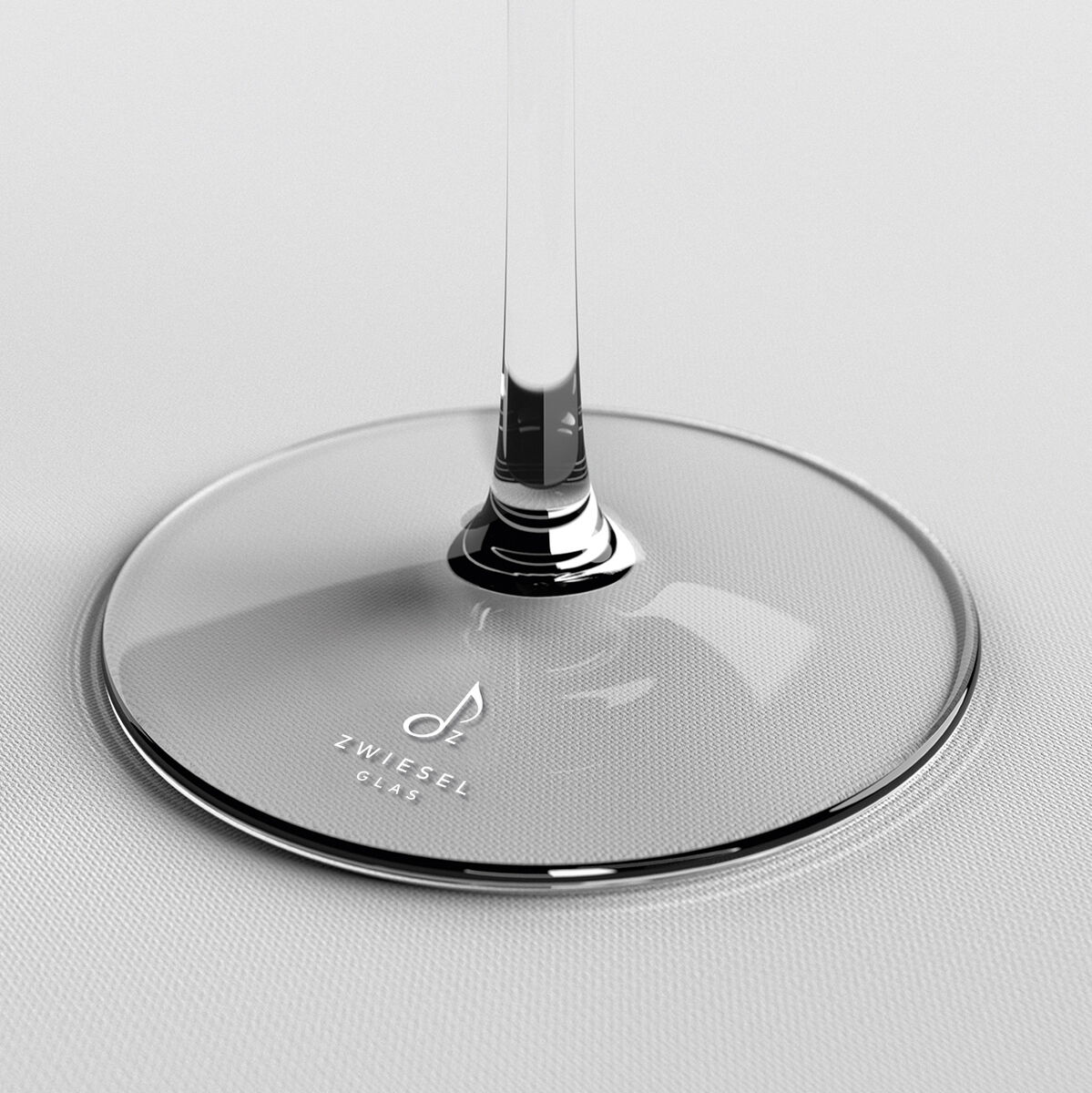 Nahaufnahme von der Basis eines Champagnerglases mit der Aufschrift 'Zwiesel Glas' auf einer weißen Oberfläche.