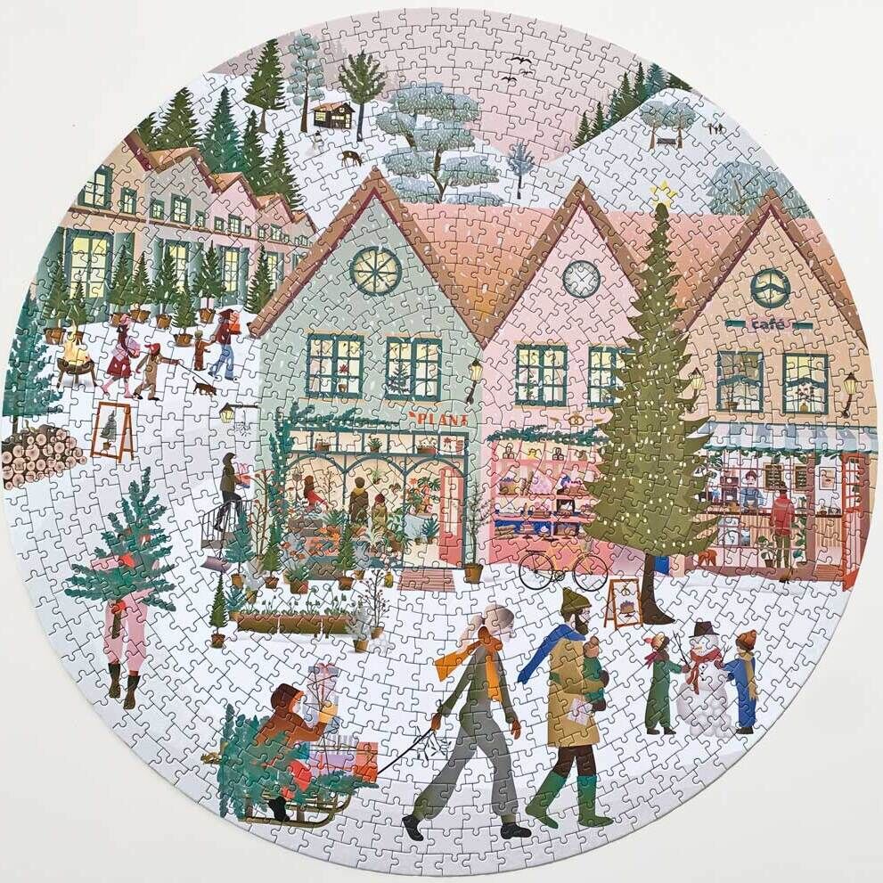 Ein rundes Puzzle mit einer winterlichen Weihnachtsszene. Es zeigt ein verschneites Dorf mit mehreren Häusern im Hintergrund, Menschen, die spazieren gehen und sich unterhalten, sowie Kinder, die im Schnee spielen. Die Farben sind hauptsächlich weiß, rosa, grün, rot und braun.