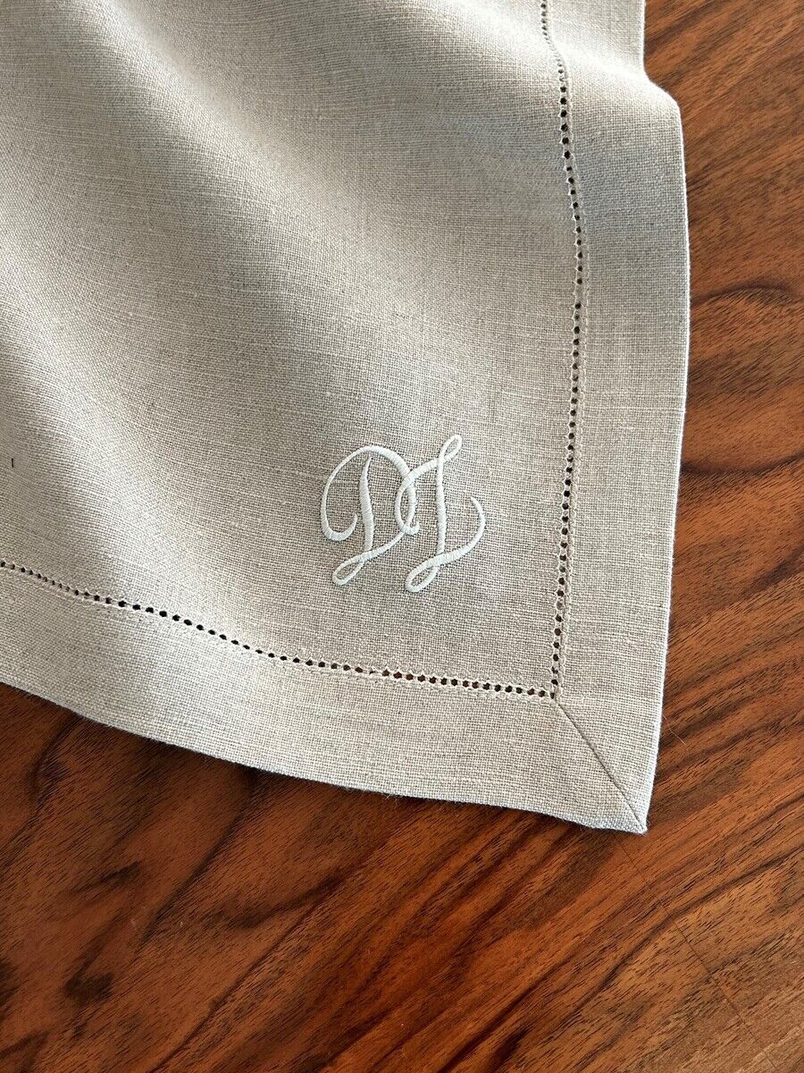Leinenserviette aus naturfarbenem Stoff mit einem gestickten Monogramm in der Ecke auf einer Holztischplatte.