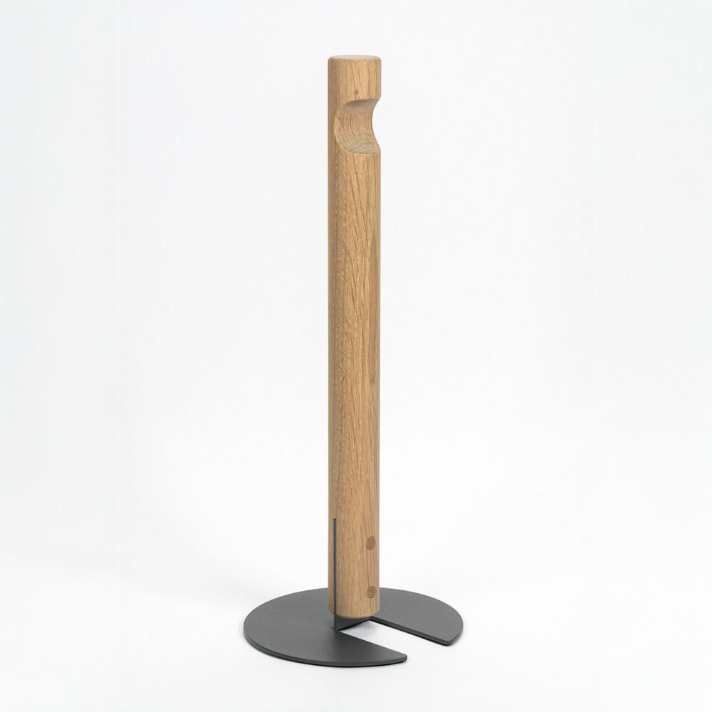 Freigestellte Produktaufnahme des Küchenrollenhalters GIVE von finbeaux vor weißem Hintergrund. Ein schlanker, senkrechter Stab aus hell gemasertem Holz mit abgerundeter Kerbe im oberen Bereich steht auf einem flachen, anthrazitgrauen Metallfuß in asymmetrischer, dreiflügeliger Form.