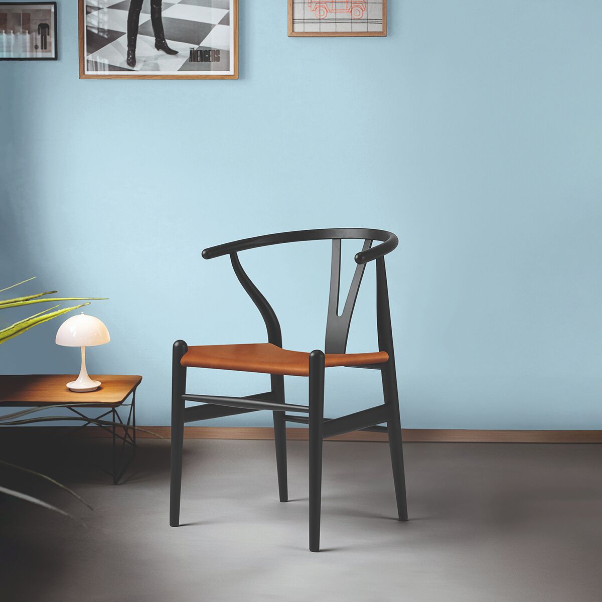 Ein stilvoller Designstuhl aus Buche und Leder, auch bekannt als Wishbone Chair, in einem minimalistisch eingerichteten Raum mit hellblauer Wand, einem niedrigen Tisch mit Tischleuchte und Bodenpflanze.