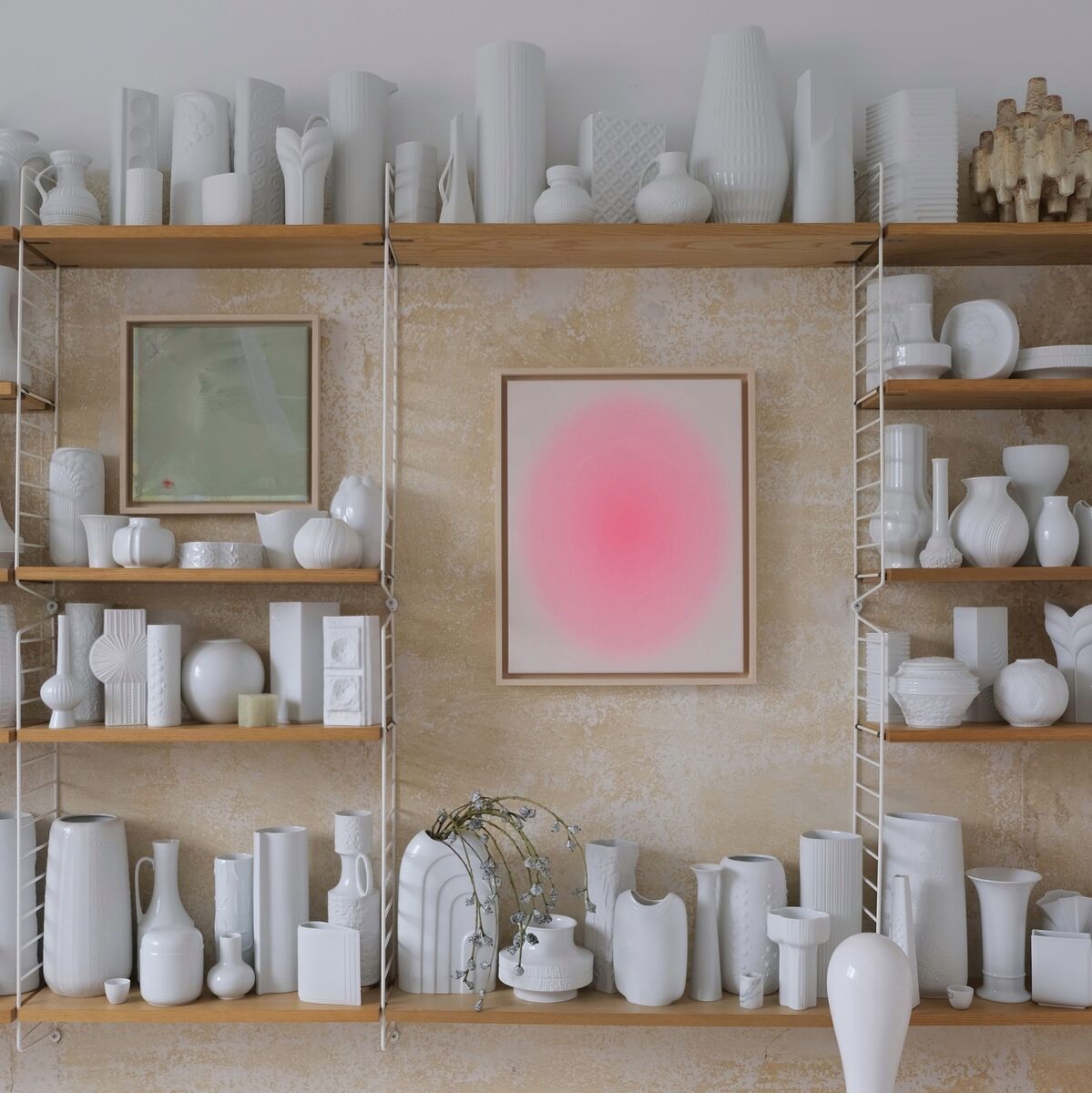 Ein modernes Kunstwerk mit dem Titel 'ZEIT-Sonderedition Sorbet Pink', dargestellt in einem minimalistischen Raum, umgeben von weißen Keramikvasen und Skulpturen auf Regalen. Das Bild zeigt einen sanften Farbübergang in Pink, gerahmt in Holz, vor einer hellen, strukturierten Wand.