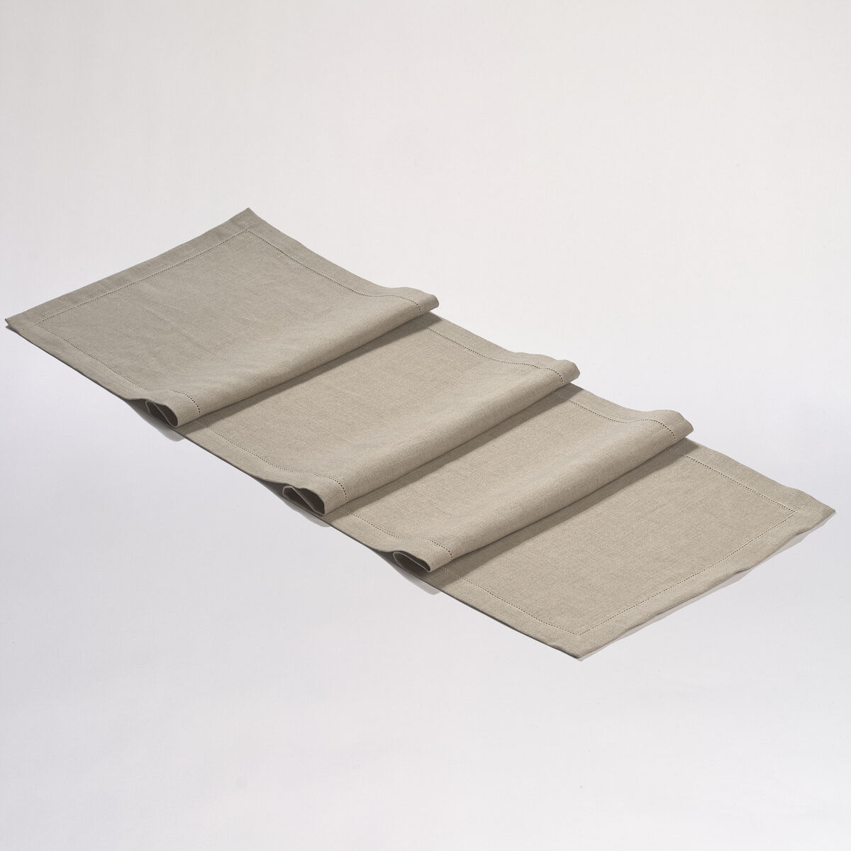 Ein beige-grauer Leinen-Tischläufer auf weißem Hintergrund. Der Tischläufer ist gefaltet und besteht aus natürlichem Leinenstoff, der eine rustikale und minimalistische Atmosphäre schafft.