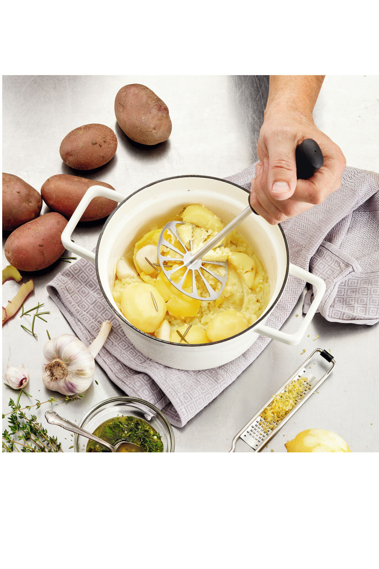 Detaillierte Nahaufnahme eines hochwertigen Kartoffelstampfers namens Soul der Marke triangle, gefertigt aus glänzendem Edelstahl mit ergonomischem kirschrotem Holzgriff. Das Design wirkt modern und edel, geeignet für stilbewusste Küchenliebhaber.