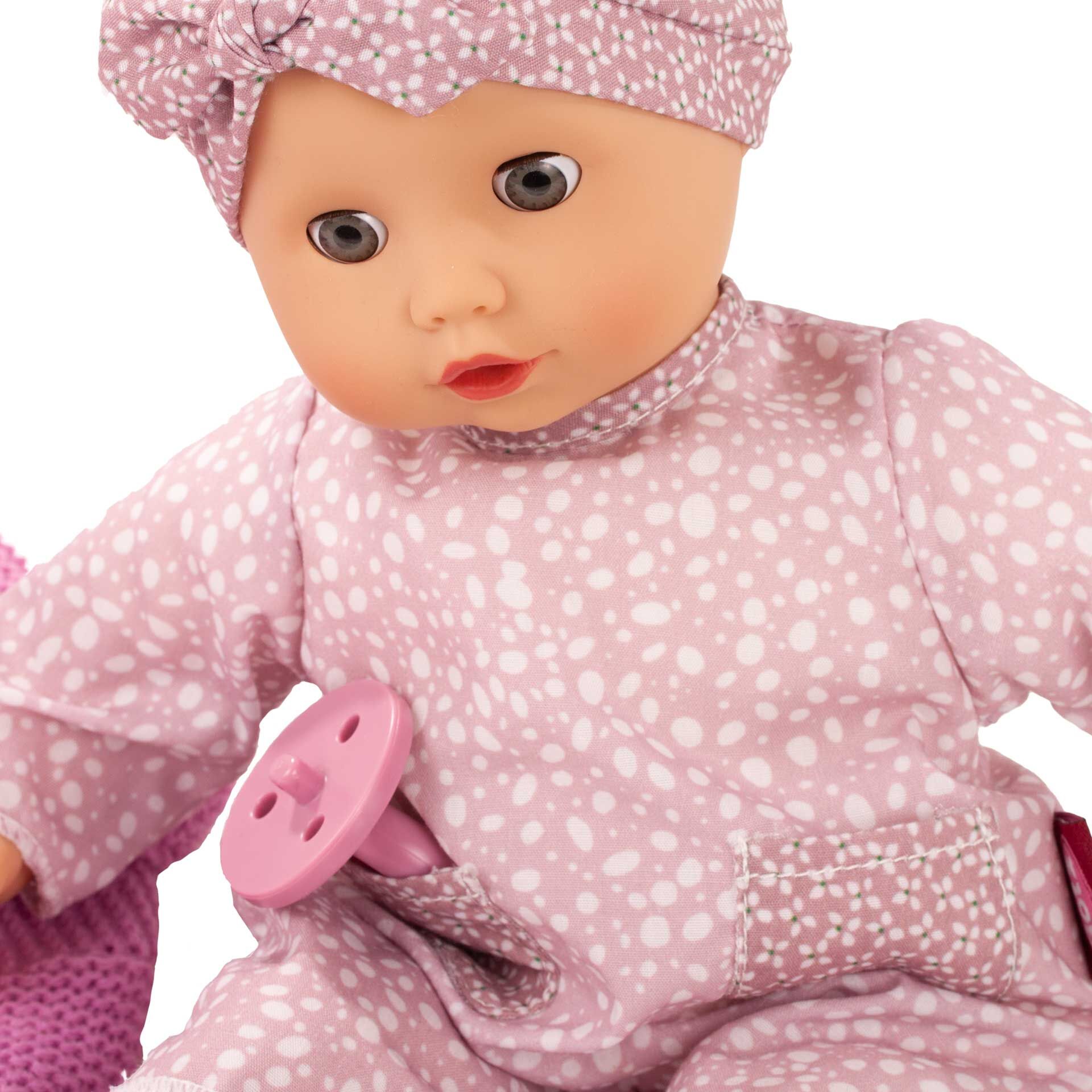 Eine weiche Babypuppe mit rosa gemustertem Strampler und passender Mütze. Die Puppe hält einen rosa Schnuller und sitzt auf einer hellen Oberfläche. Diese Kuschelpuppe eignet sich ideal für Kleinkinder und als Geschenk zu besonderen Anlässen.