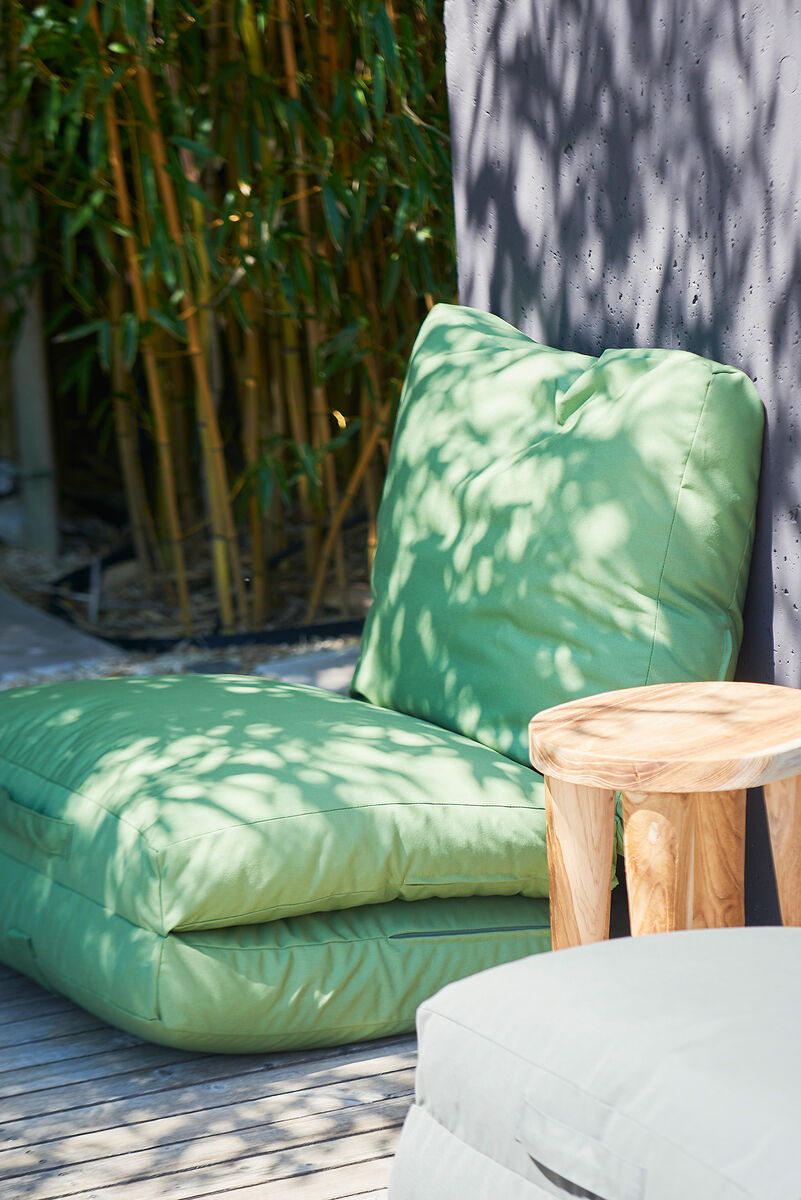 Eine grüne Gartenmatratze »Sheffield« mit Rückenstütze neben einem kleinen Holztisch auf einer Terrasse mit Bambus im Hintergrund.